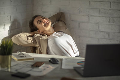 Smiling young caucasian female manager sitting at the table stretching her arms. work-life-balance