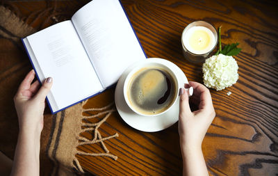 Cropped hands of woman holding book and coffee cup on table