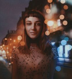 Portrait of young woman standing in illuminated city at night