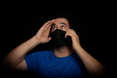 Portrait of man covering face against black background