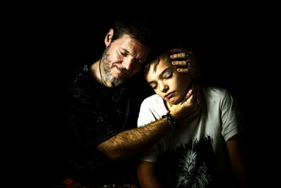 Close-up of father and son with eyes closed against black background