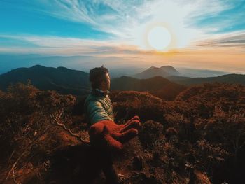 Woman sitting on mountain against sky during sunset