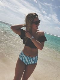 Beautiful woman standing at beach against sky