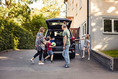 Family standing by electric car with open trunk in back yard