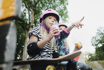 Girl pointing and showing to friend while having juice at skateboard park