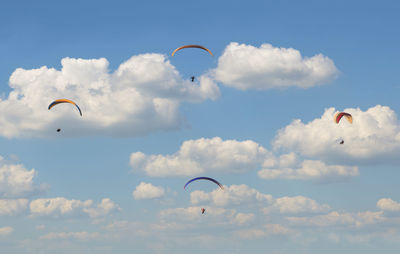 Low angle view of people paragliding against sky