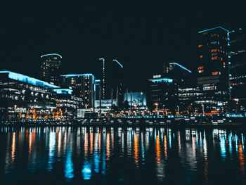 Illuminated buildings by river against sky at night