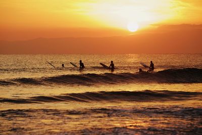 Silhouette people in sea against sky during sunset