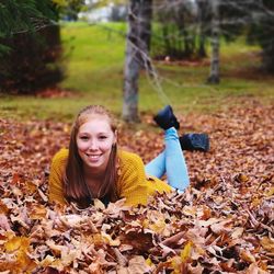 Portrait of smiling young woman lying on autumn leaves in park