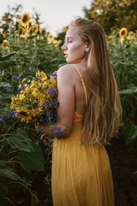 Young woman looking down while standing on yellow flowering plants