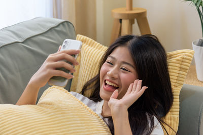 Young woman using mobile phone while lying on bed at home