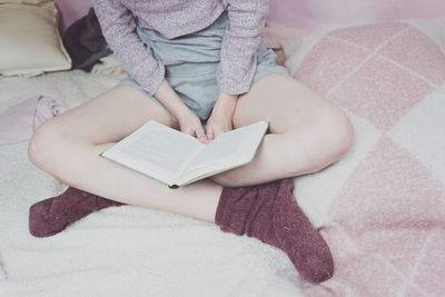 Low section of woman reading book while sitting on bed
