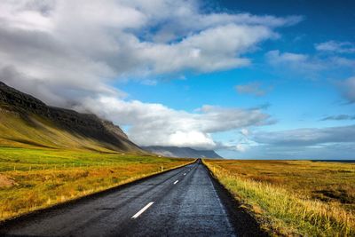 Road passing through field against cloudy sky