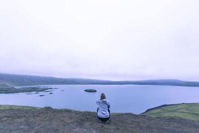 Woman sitting taking photograph of lake in highlands iceland at sunset