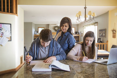 Mother looking at children studying on table at home