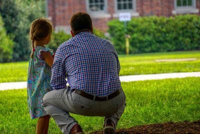 Rear view of father crouching while daughter standing on field