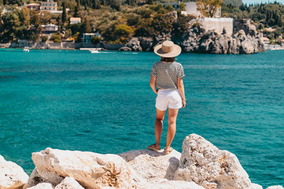 Rear view of woman standing on rock by sea