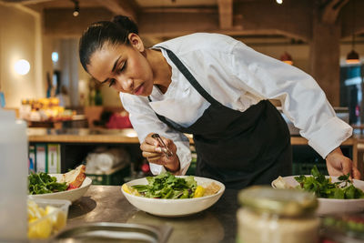 Female chef garnishing salad using tweezers in commercial kitchen