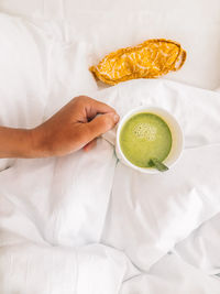 Cropped hand holding matcha tea on bed