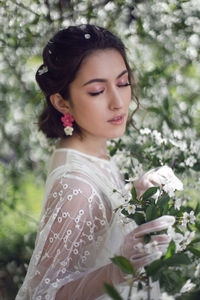 Portrait of a young beautiful woman in white clothes standing next to blooming cherry tree in spring