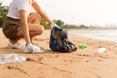 Low section of woman tying shoelace on sand at beach