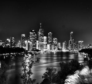 Illuminated cityscape by river against sky at night