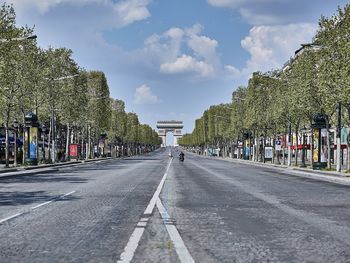 Road by trees in city against sky
