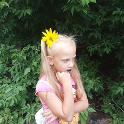 Girl with hand on chin wearing flower while standing at park