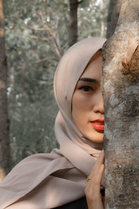 Close-up portrait of a young woman against tree trunk