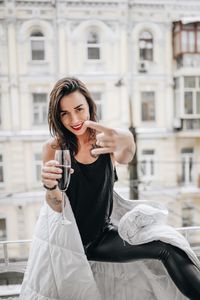 Portrait of cheerful woman having red wine while wrapped in blanket at balcony