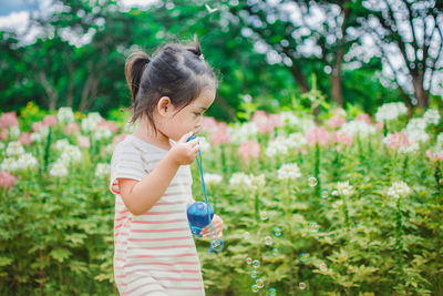 Girl holding bubble wand by flowers at park