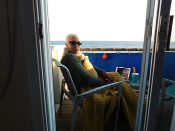Portrait of mature woman wearing sunglasses while sitting on balcony by sea