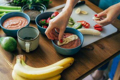 Female hands lay out sliced fruits on a bowl with pink chia pudding. ugly food. 