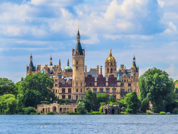 Buildings by river against cloudy sky