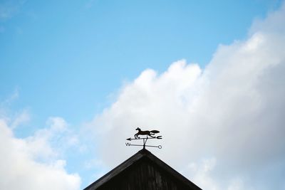 Low angle view of weather vane on house pediment against sky