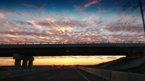 Bridge over highway against sky during sunset