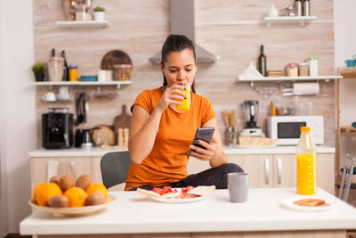 Full length of woman holding mobile phone at home