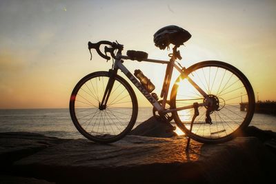 Bicycle by sea against sky during sunset