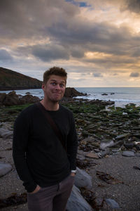 Young man standing in front of sea against cloudy sky