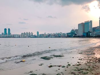 Sea by city buildings against sky during sunset