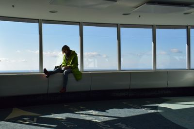 Woman sitting by window against sky