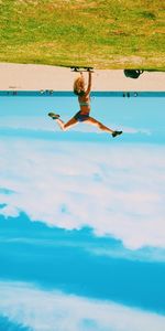 Upside down image of woman doing handstand on skateboard against sky at beach