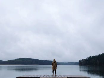 Rear view of woman standing by lake against sky