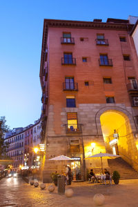 Illuminated street amidst buildings against sky at dusk