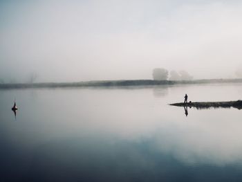 Silhouette of man standing by lake during foggy weather