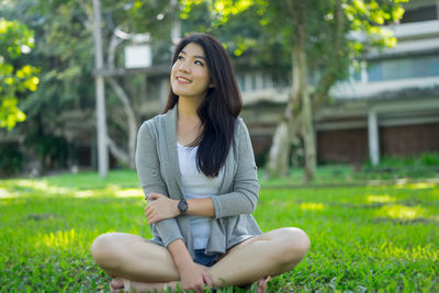 Smiling young woman sitting on field against trees