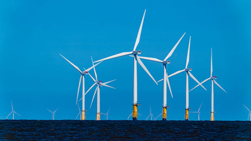 Wind turbines by sea against clear blue sky