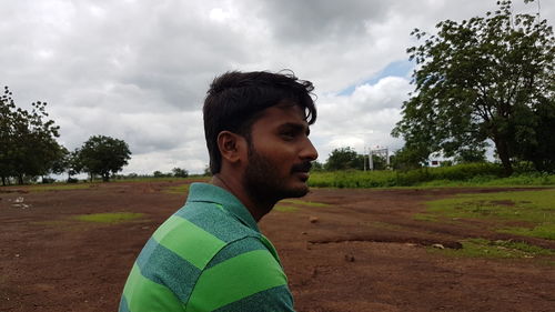 Side view of young man on field against cloudy sky