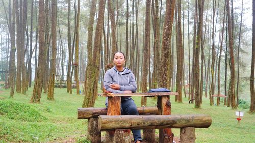 Full length of man sitting on tree trunk in forest