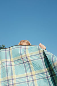 Low angle view of person holding blanket against clear blue sky